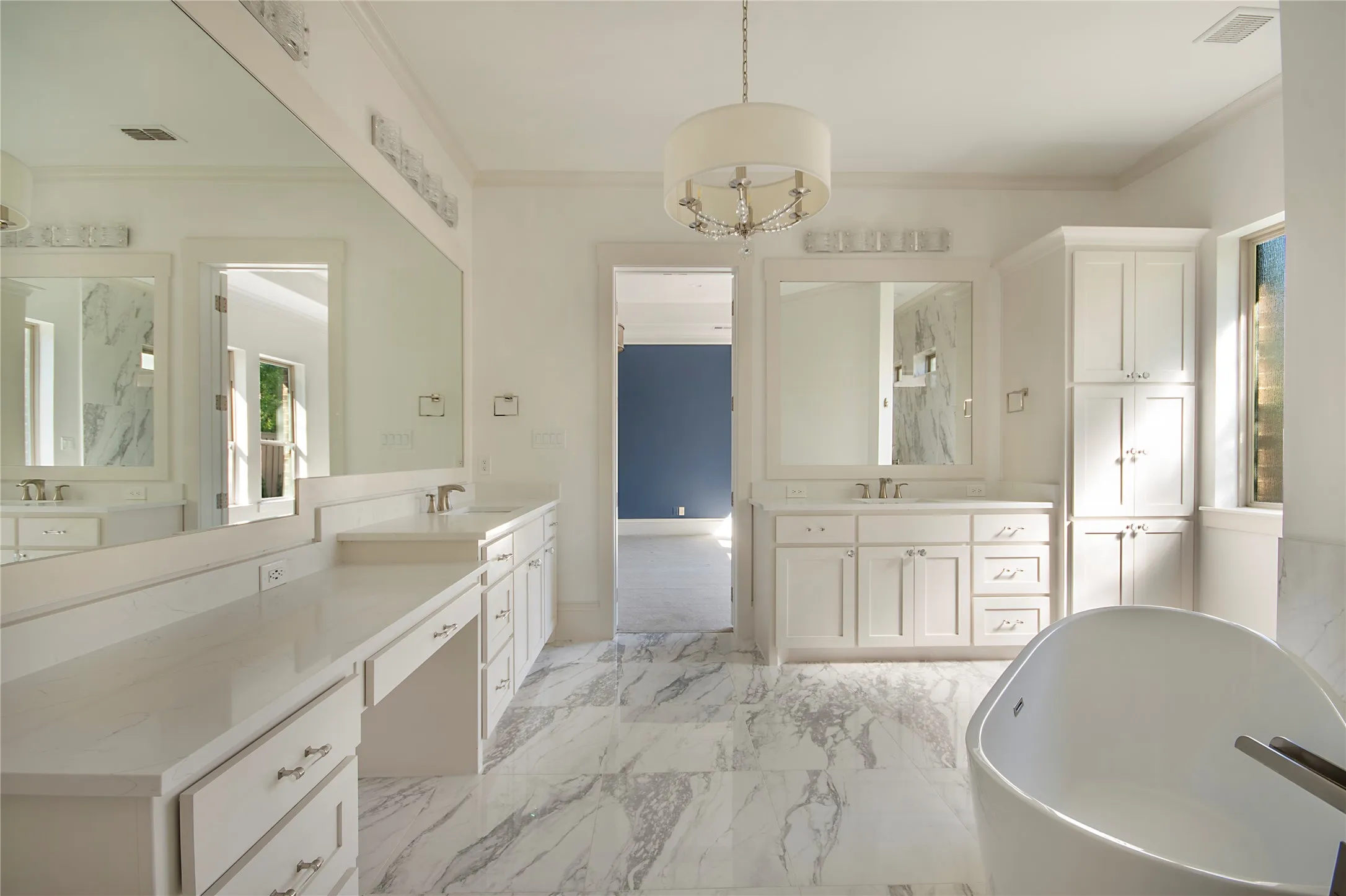 Freestanding soaking tub, dual vanities with white cabinetry, light-toned countertops, and marble-look flooring
