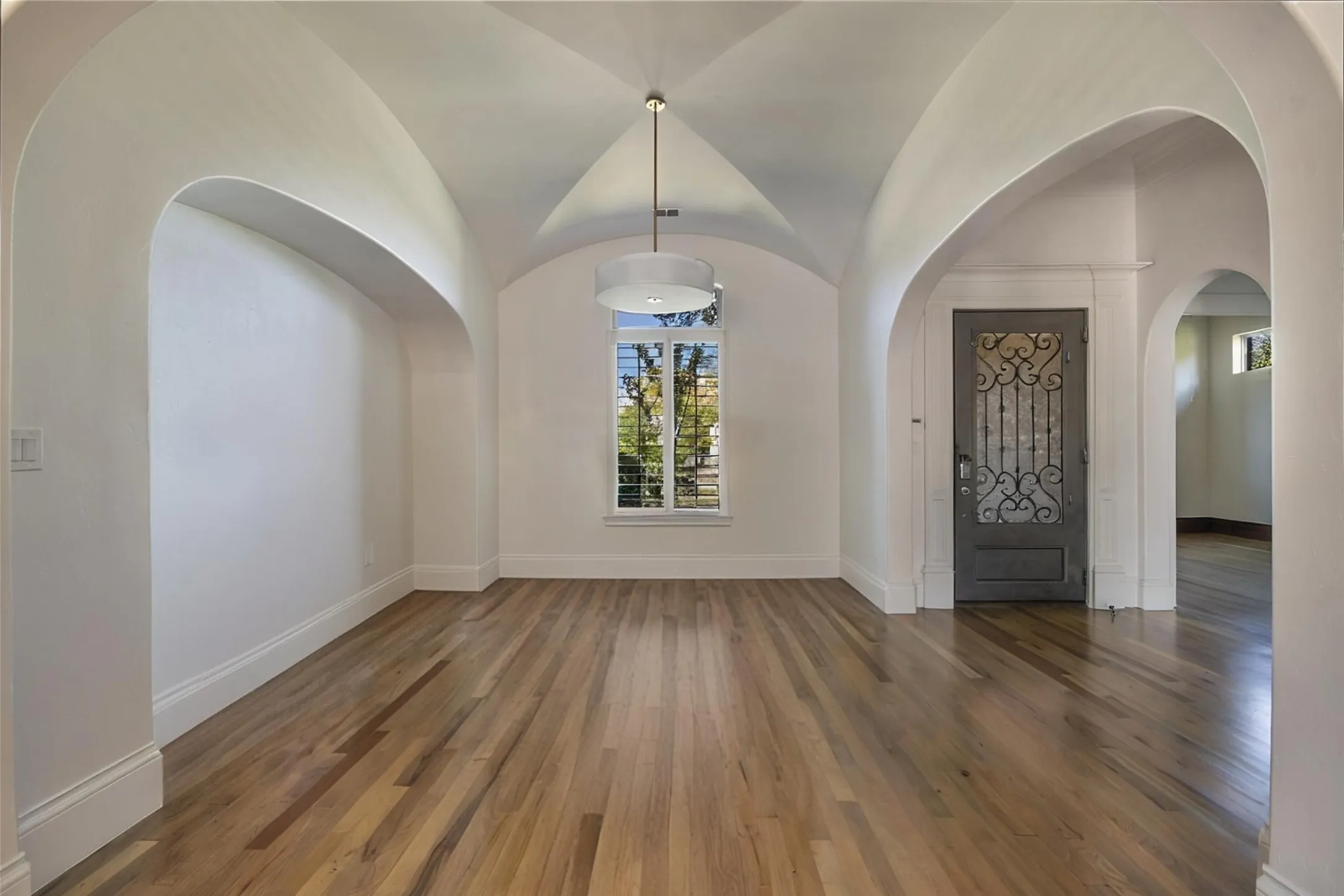 Vaulted ceiling, arched doorways, wood-finish flooring, central window, and an ornate entry door