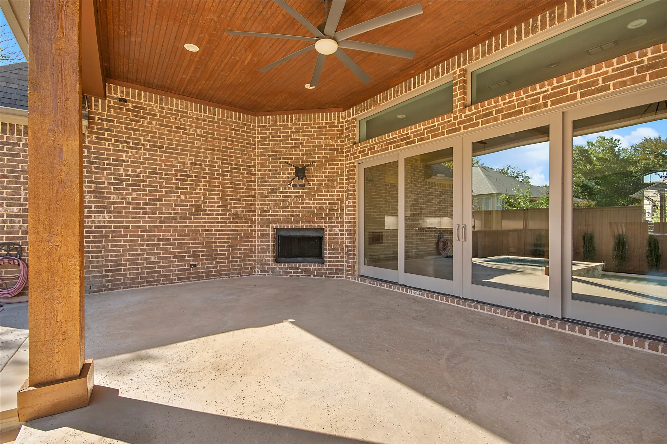Covered patio with a wood-paneled ceiling, ceiling fan, and brick fireplace