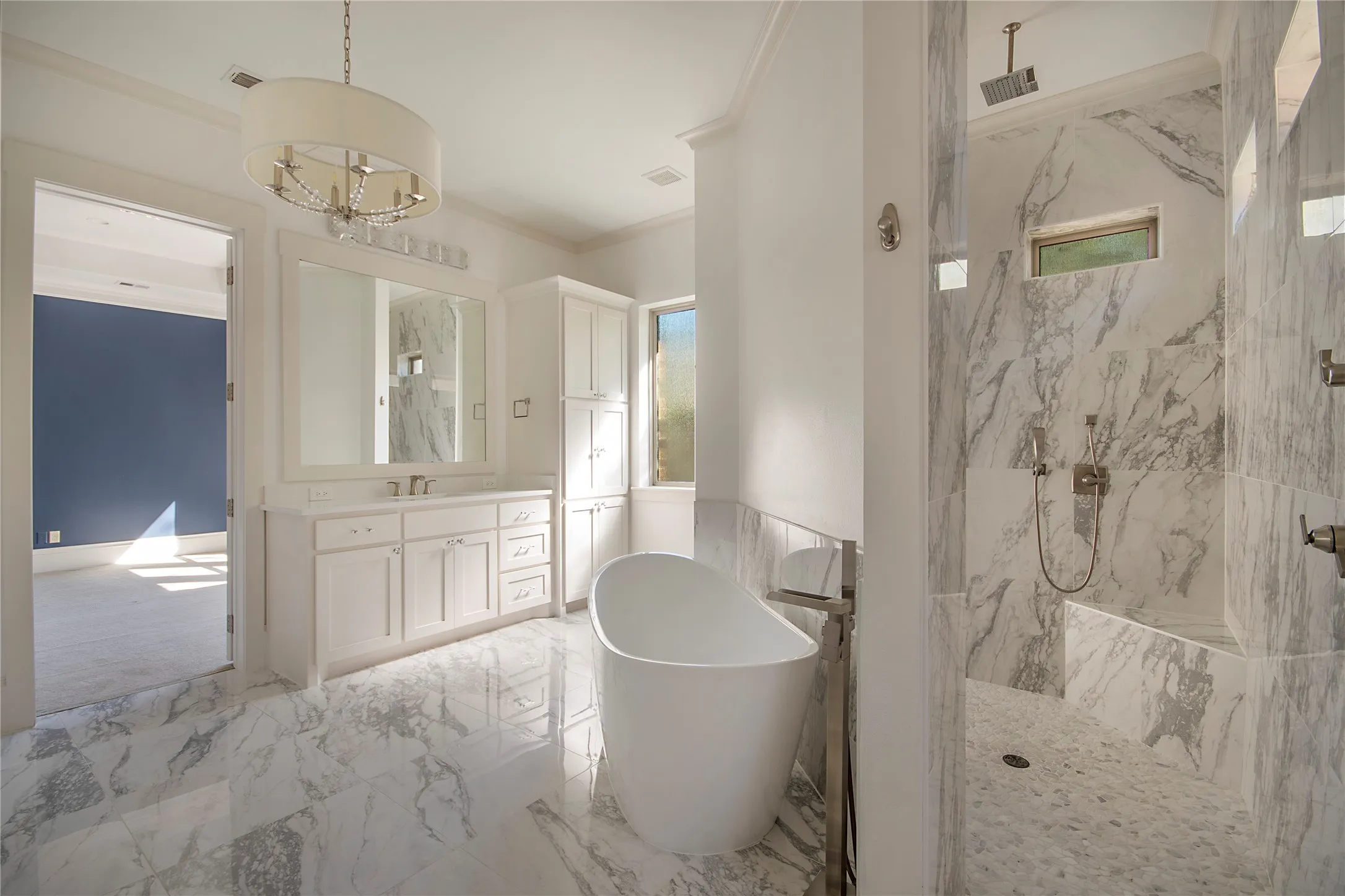Spacious bathroom featuring a freestanding tub, a walk-in shower with a built-in bench, a double vanity, and marble-look tile flooring