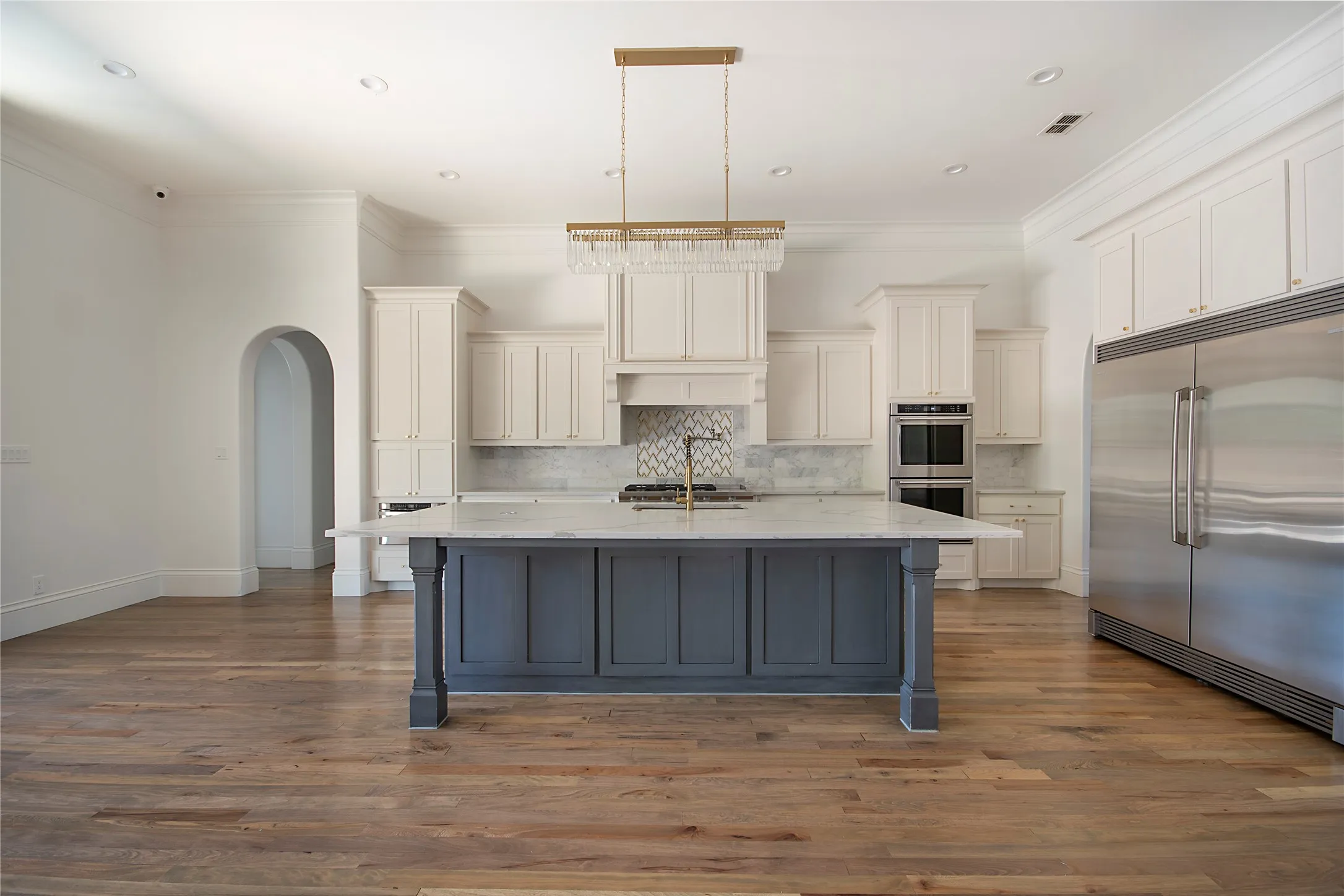 Gourmet kitchen featuring a large central island with seating, stainless steel double ovens, a built-in refrigerator, and wood-finish flooring