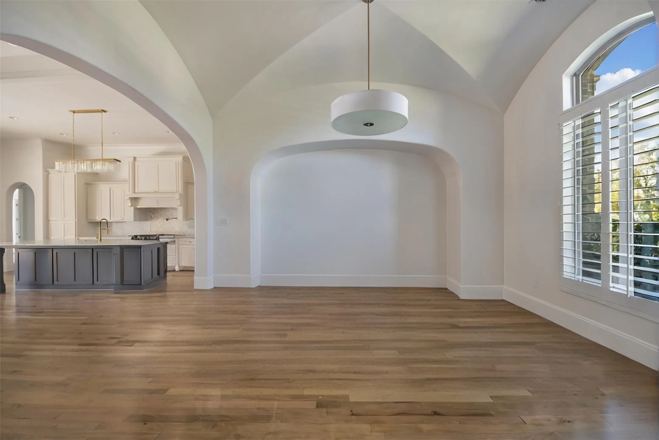Vaulted ceiling with an arched entry, wood-finish flooring, built-in wall niche, and plantation shutters