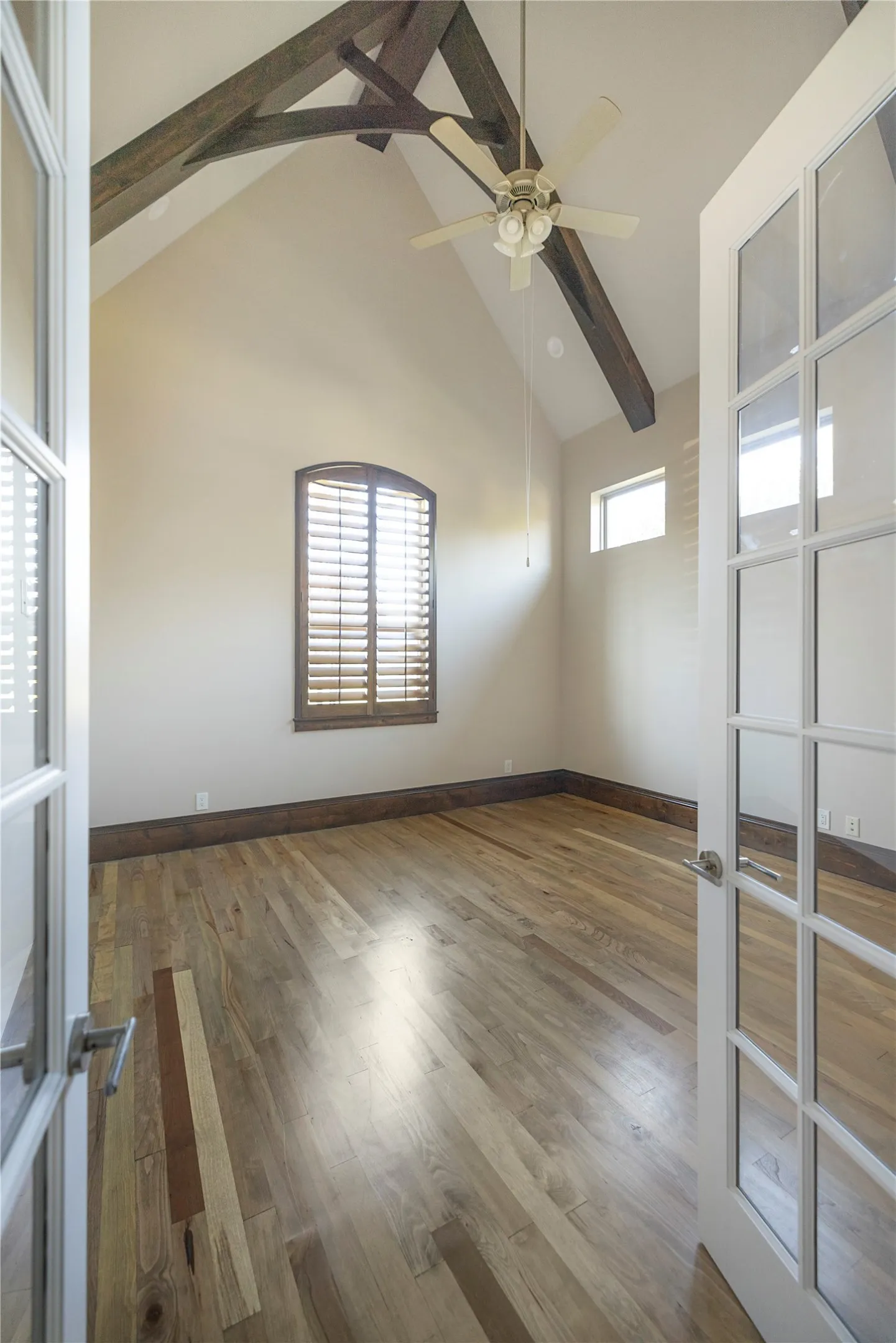 Vaulted ceiling with exposed wood beams, wood-finish flooring, and a ceiling fan with light fixture