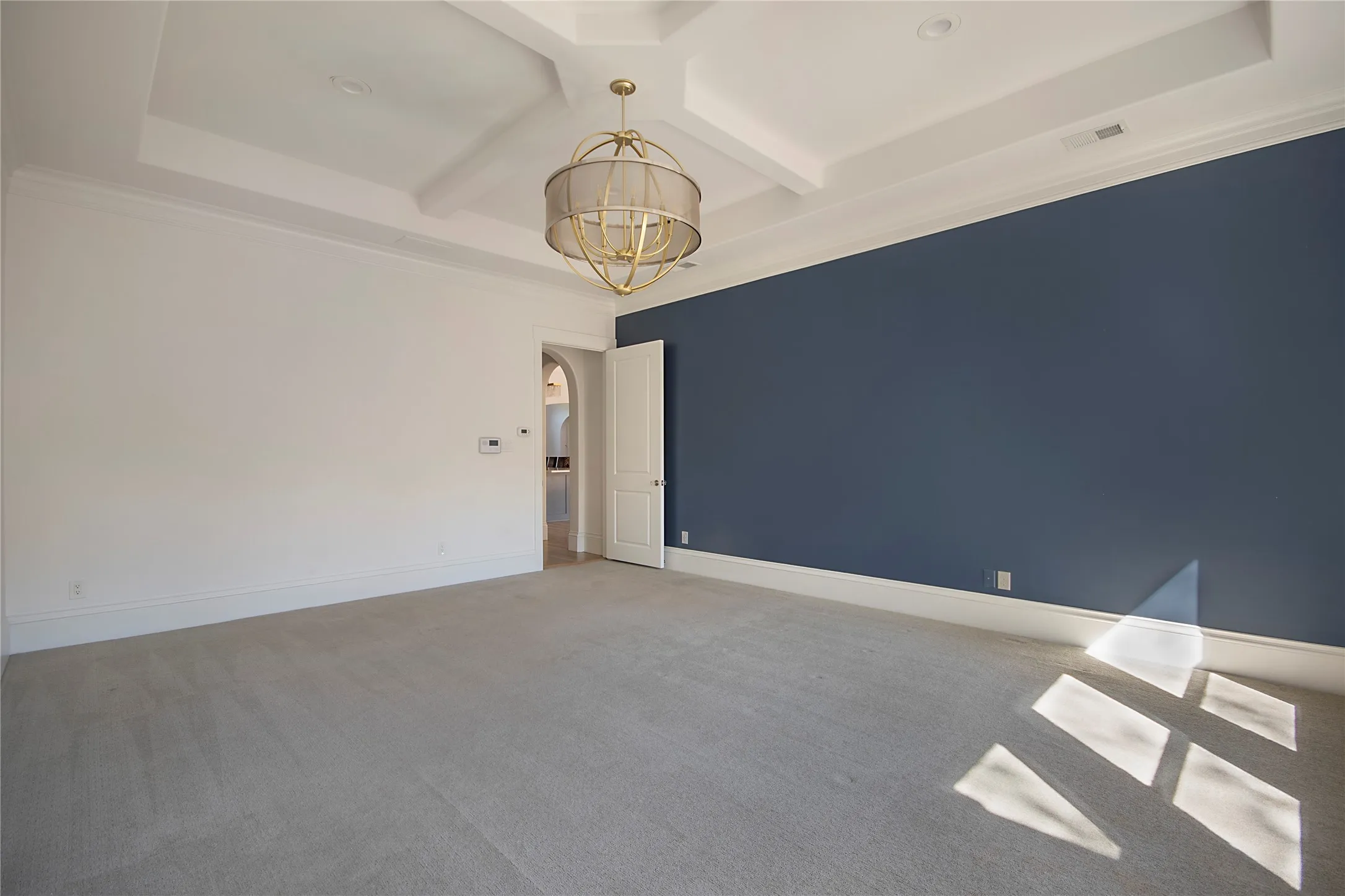 Coffer ceiling with recessed lighting, decorative chandelier, dark accent wall, carpeted flooring, and an arched doorway