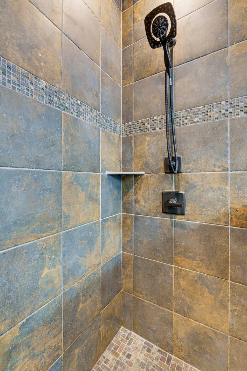 Shower with large format wall tiles, a mosaic tile accent band, a built-in corner shelf, and a handheld shower head