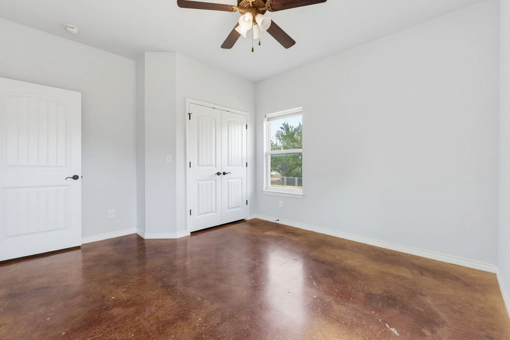 Brown-toned concrete flooring, white walls, and a ceiling fan with light fixture