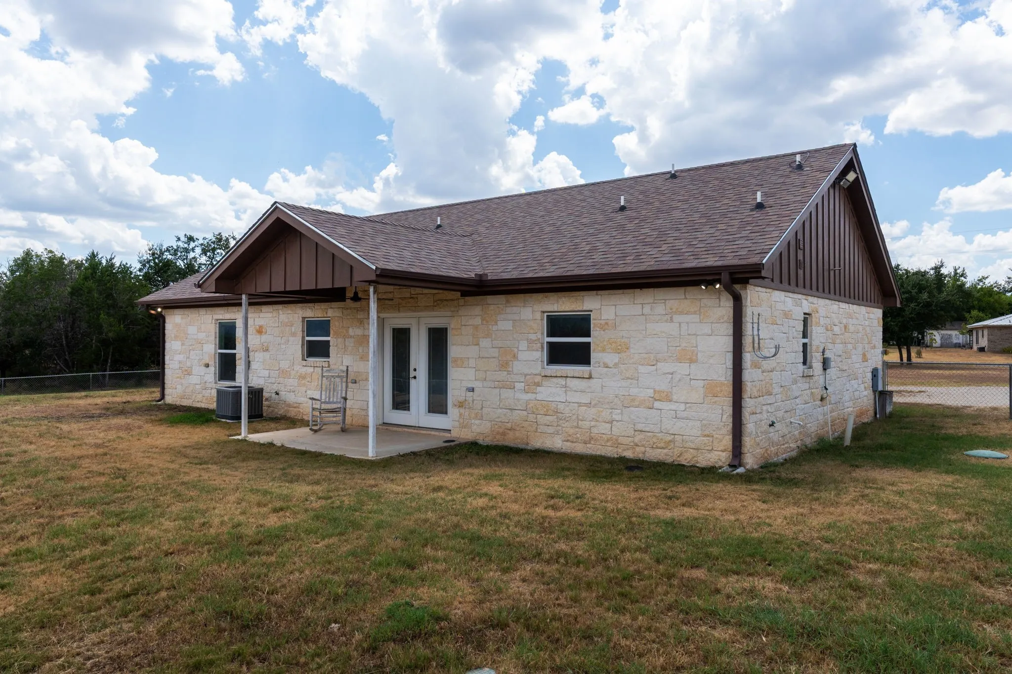 Stone exterior with a covered patio, double French doors, and a brown shingle roof