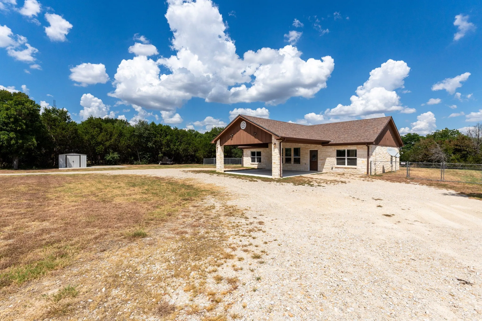 Stone exterior with a covered carport, multiple windows, and a metal storage shed