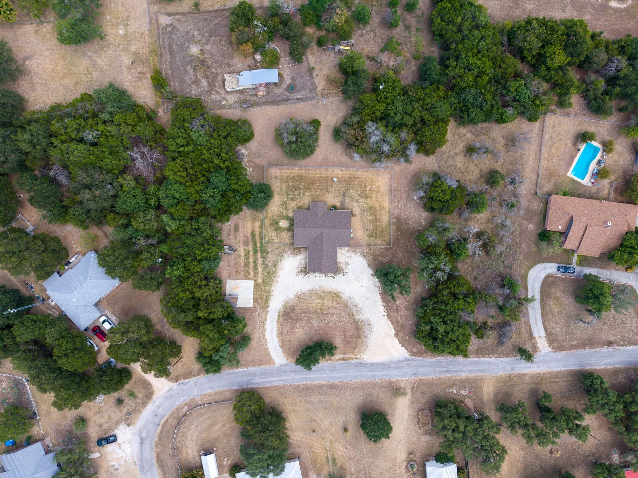 Expansive property featuring a central residence with a brown shingle roof, surrounded by numerous mature trees and a gravel driveway