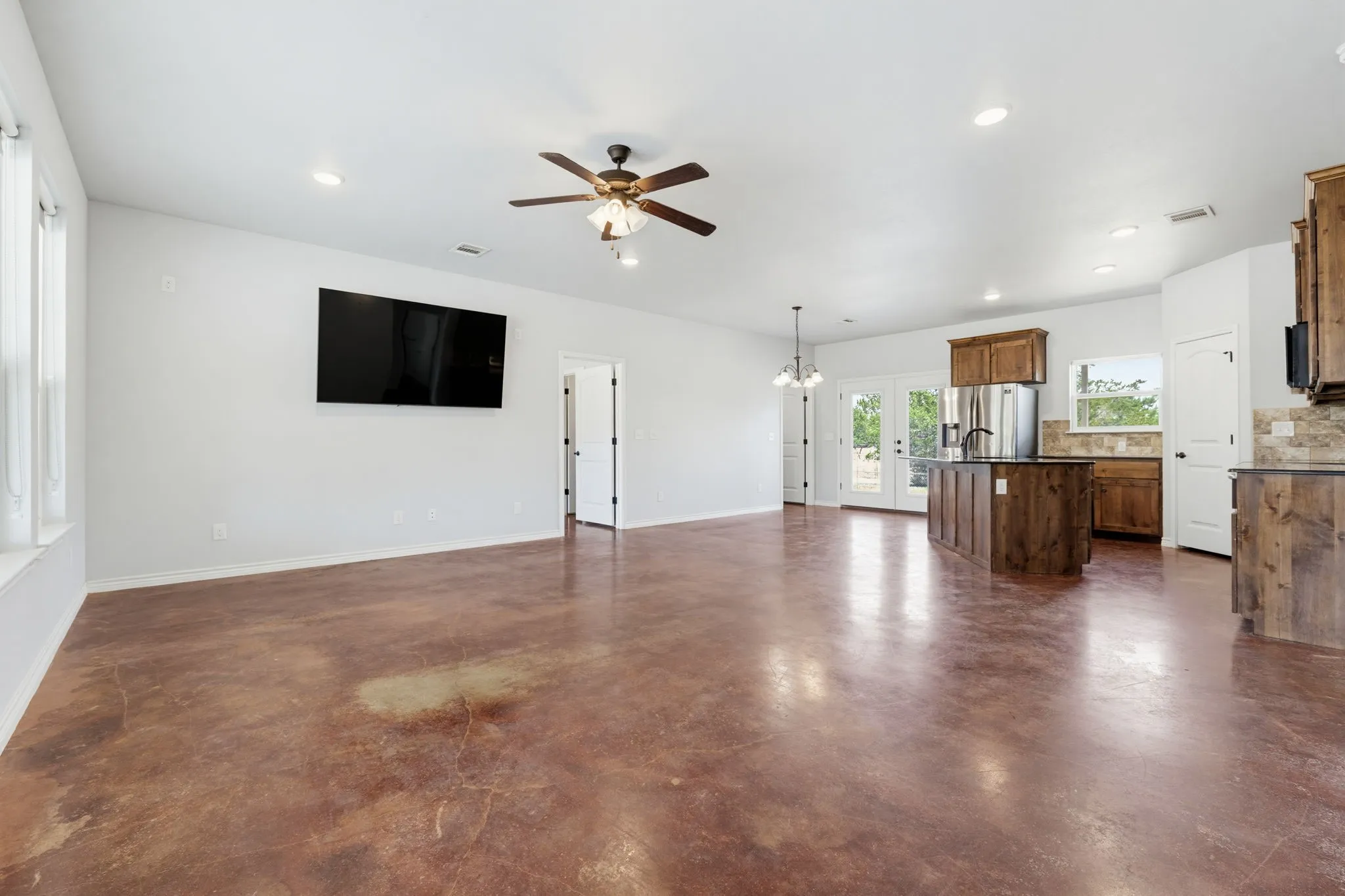 Spacious open-concept living area featuring stained concrete flooring, recessed lighting, and a ceiling fan