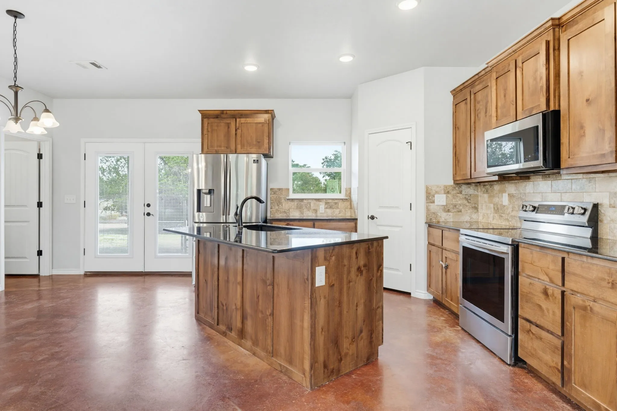 Kitchen featuring wood cabinetry, stainless steel appliances, a center island with a dark countertop, a tiled backsplash, and double glass-paneled doors