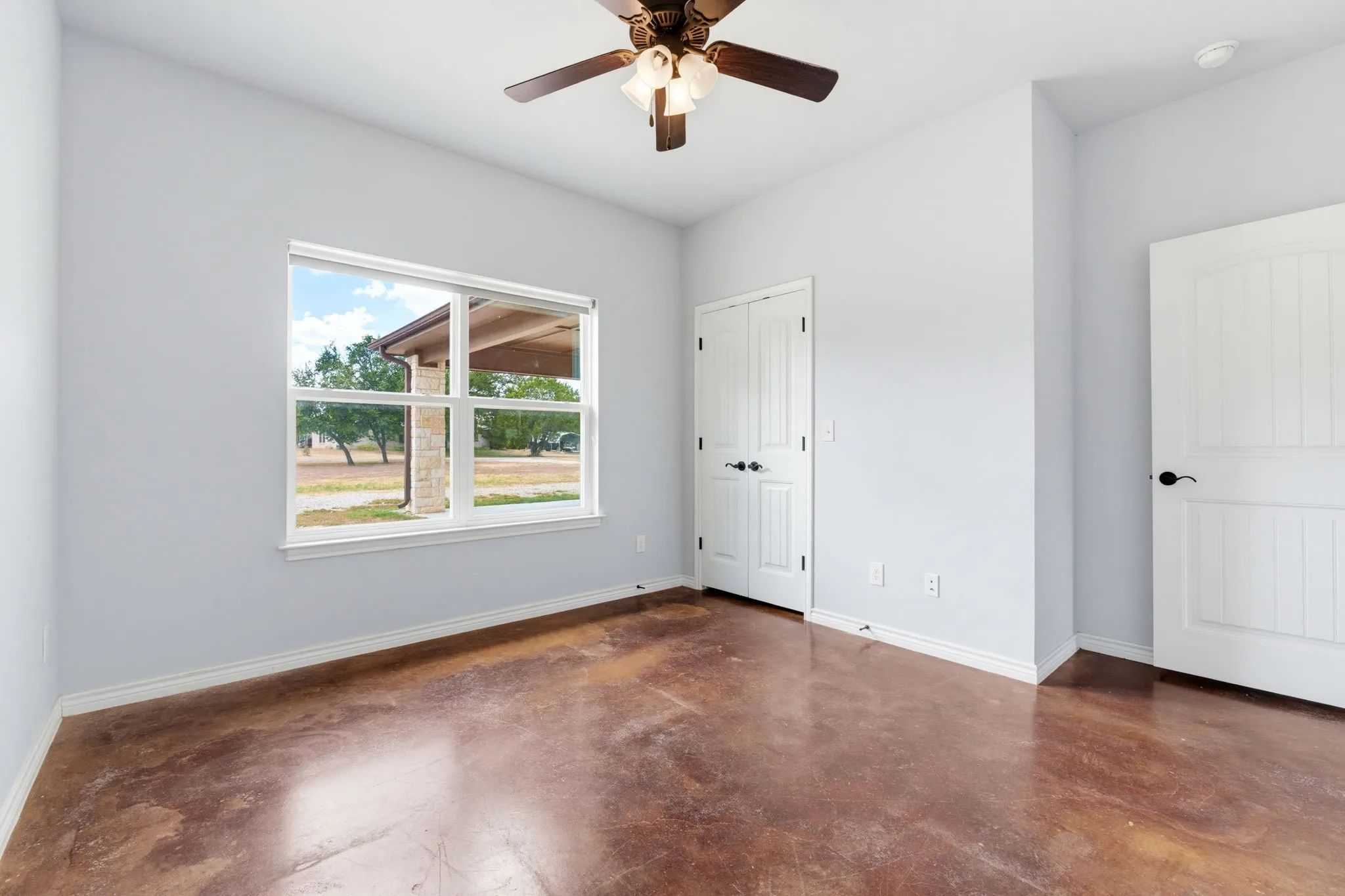 Stained concrete flooring, a ceiling fan with integrated lighting, and a white paneled door