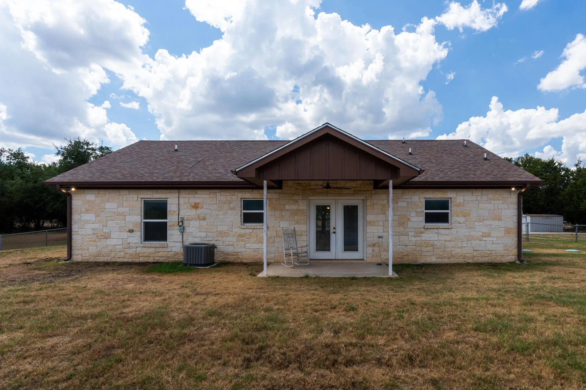Stone masonry exterior with a covered patio, double glass-paneled doors, and a shingle roof