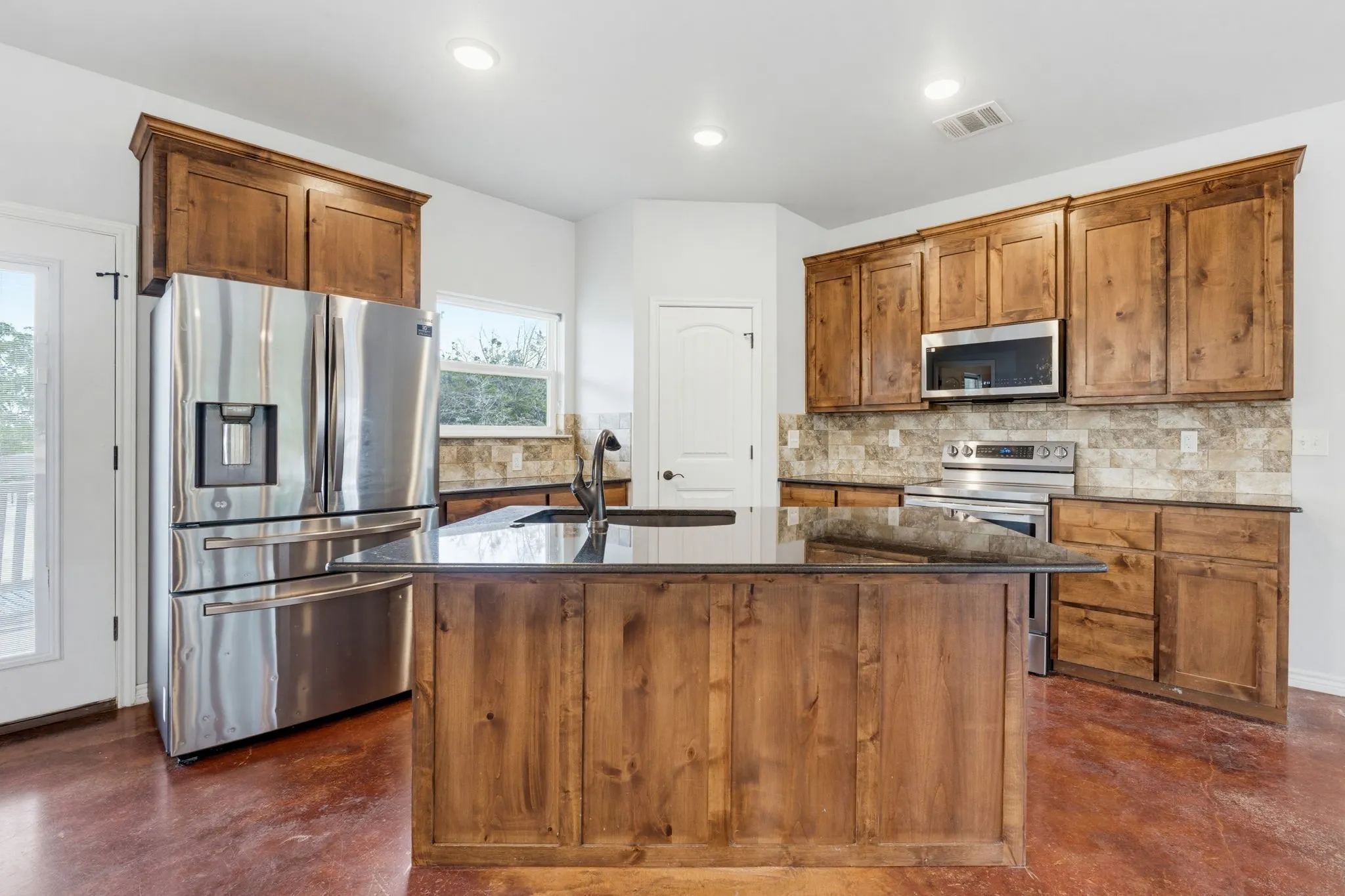 Kitchen featuring wood cabinetry, stainless steel appliances, a center island with a dark countertop, and a tile backsplash
