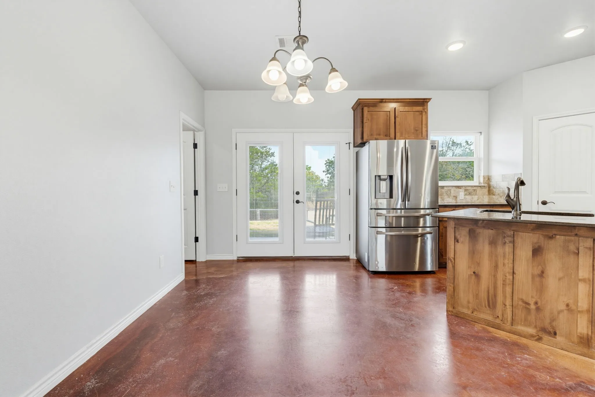 Stained concrete flooring, French doors with exterior access, stainless steel refrigerator, wood cabinetry, and a stone backsplash