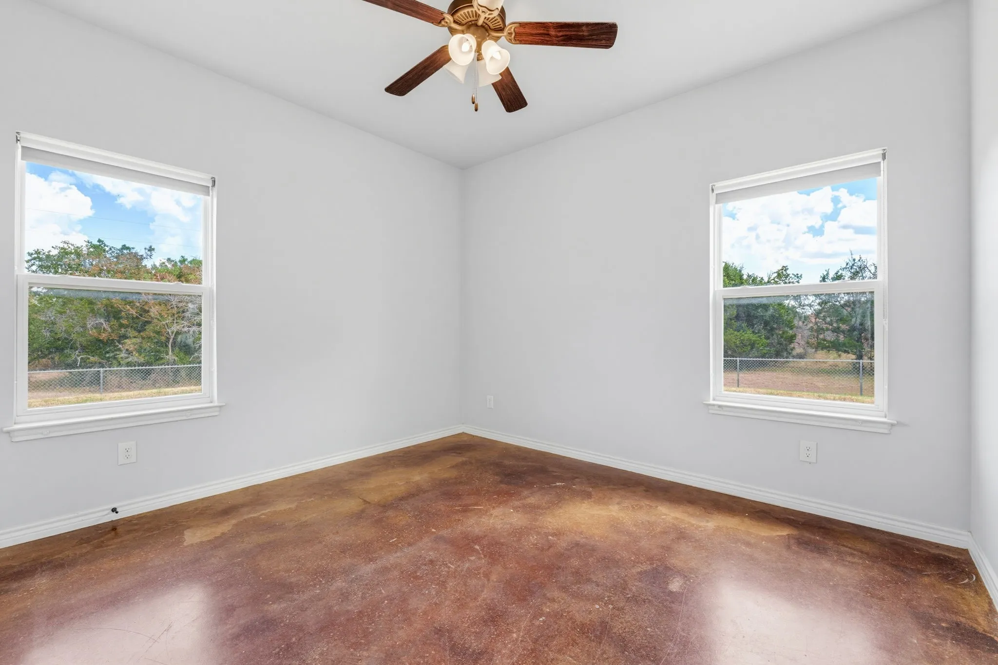 Bright interior with two single-hung windows, concrete flooring, a ceiling fan, and white walls