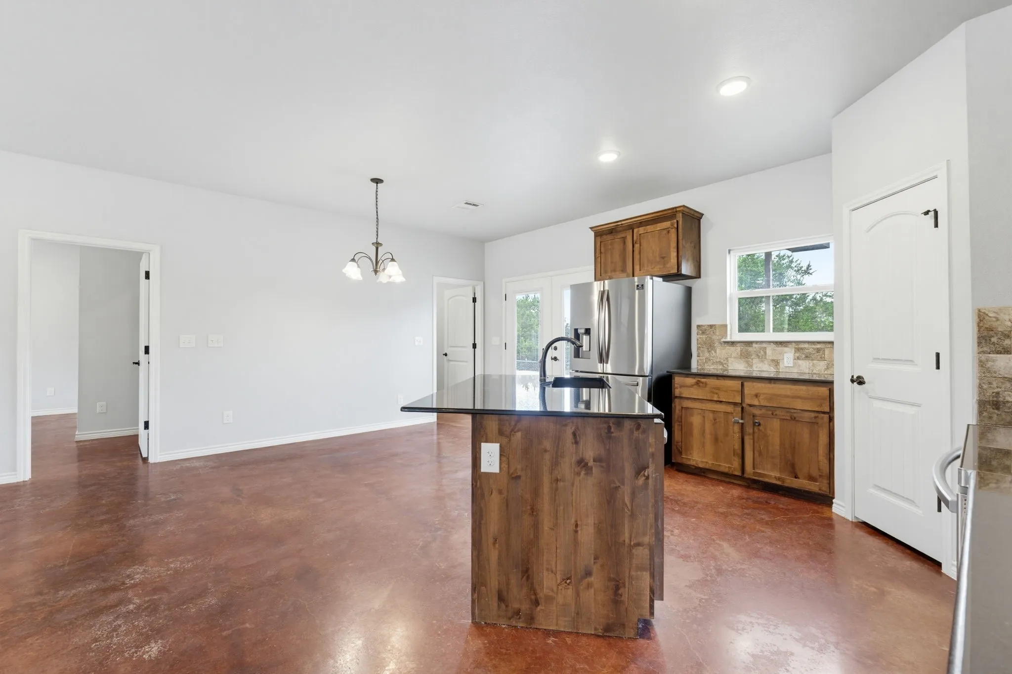 Open-concept living area featuring stained concrete flooring, recessed lighting, and a kitchen island with a dark countertop