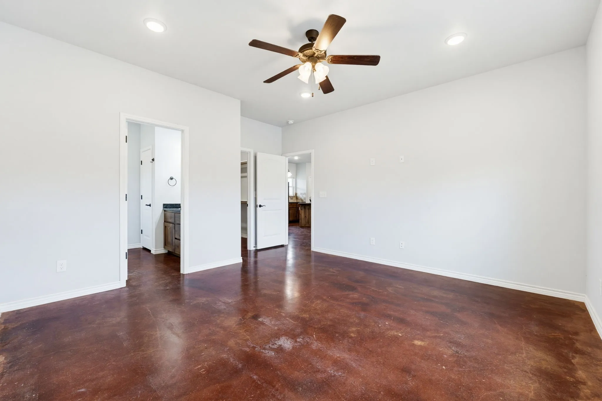 Spacious room featuring a ceiling fan with light, recessed lighting, stained concrete flooring, and white interior doors