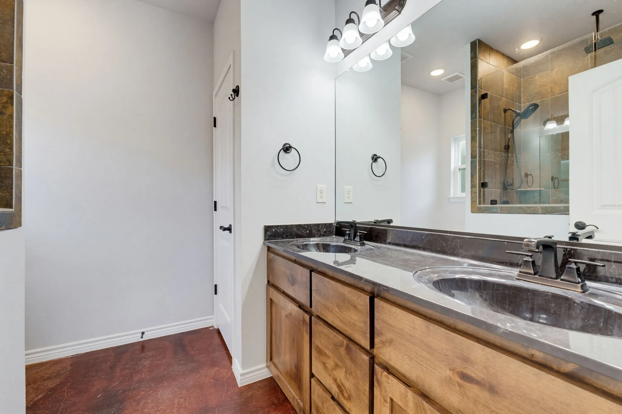 Dual vanity with dark countertops, wood-finish cabinetry, and a full-width mirror