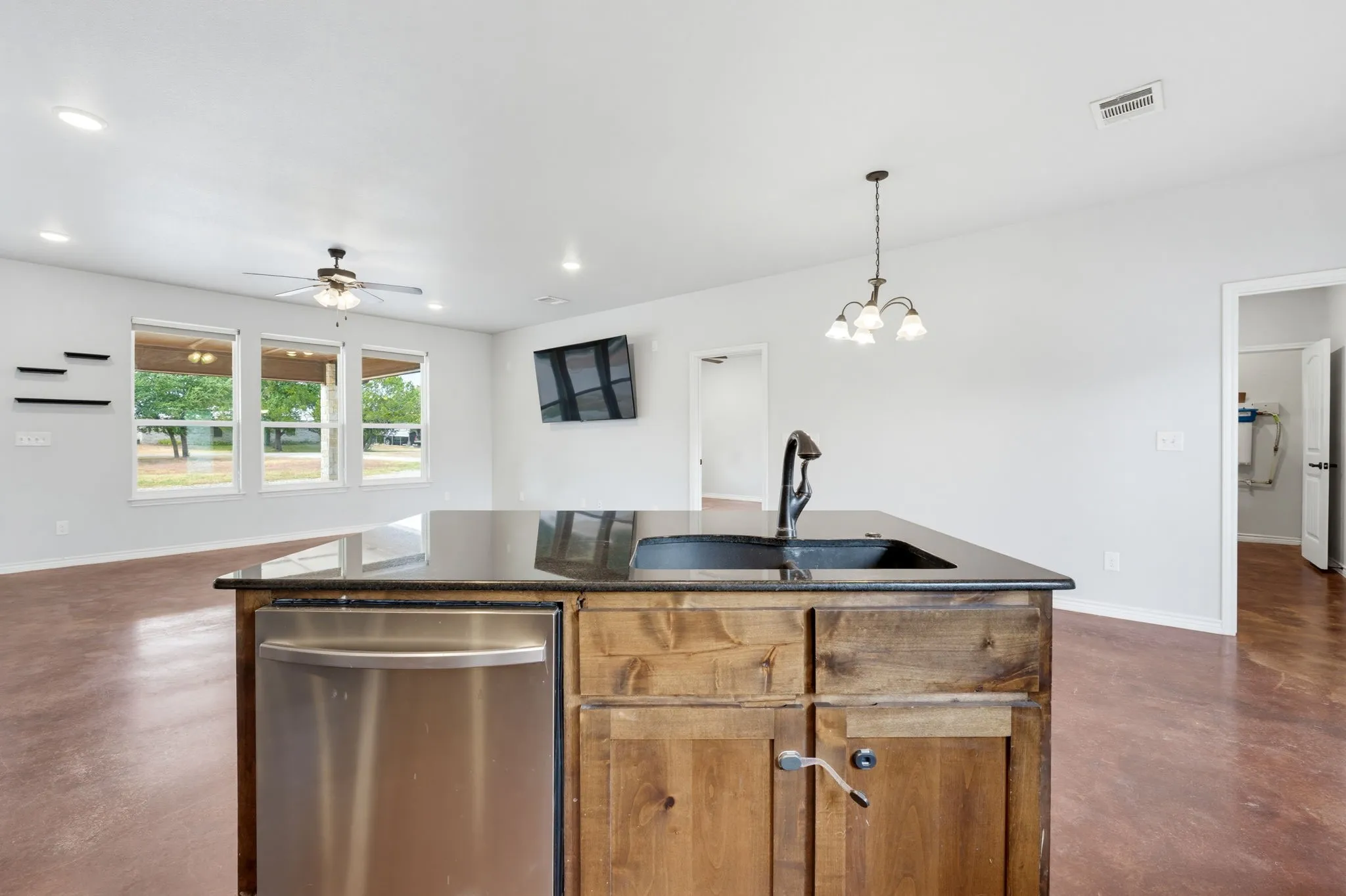 Kitchen island with a dark countertop and undermount sink, stainless steel dishwasher, wood-finish cabinetry, and a bronze chandelier