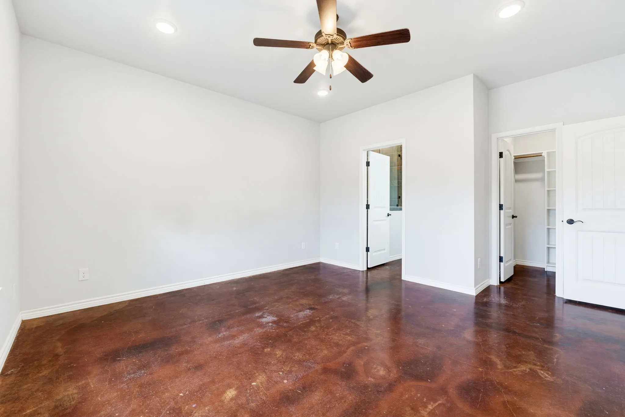 Expansive room featuring stained concrete flooring, a ceiling fan with light fixture, recessed lighting, and white paneled doors with dark hardware