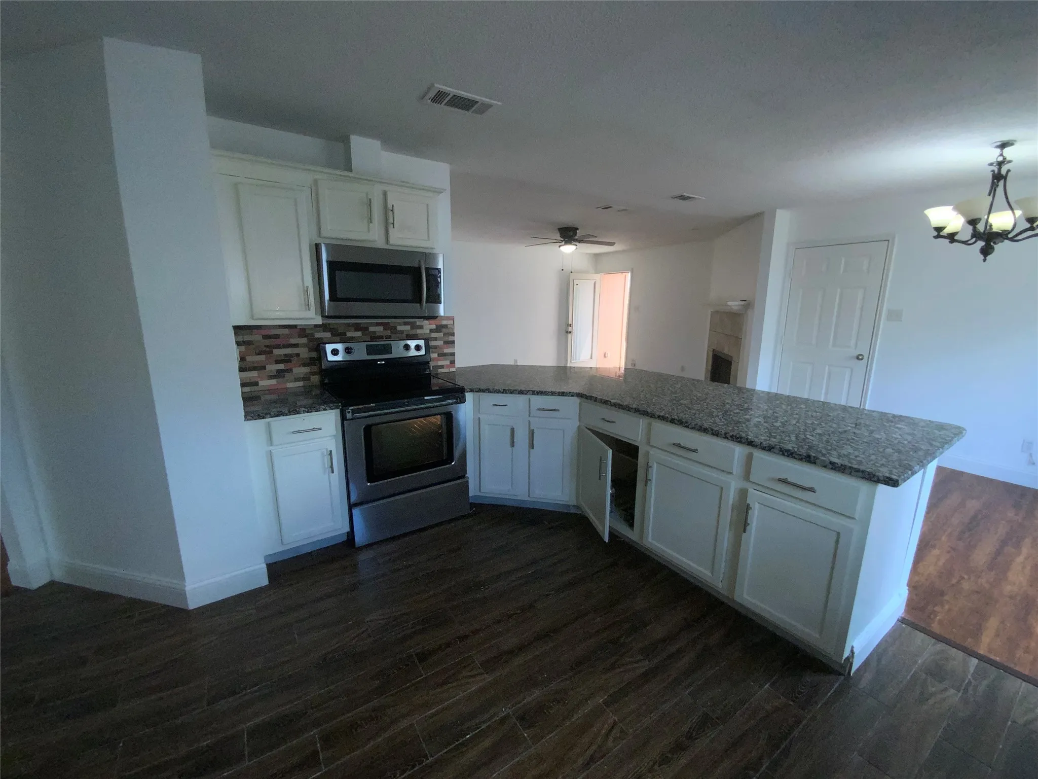Kitchen featuring white cabinetry, stainless steel appliances, a multi-tone tile backsplash, and a large island with a speckled countertop