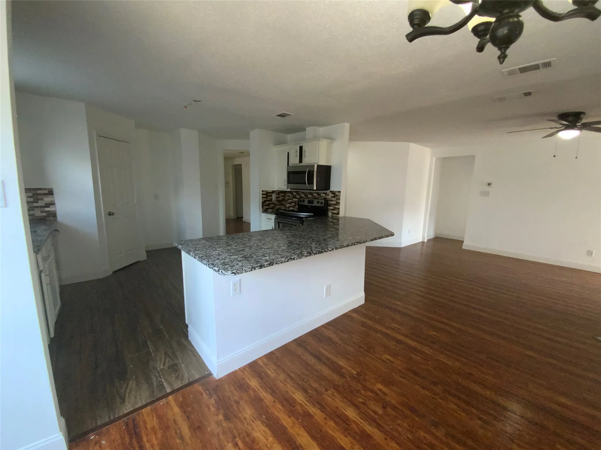 Kitchen island with a granite-style countertop, tile backsplash, stainless steel microwave, wood-finish flooring, and a ceiling fan