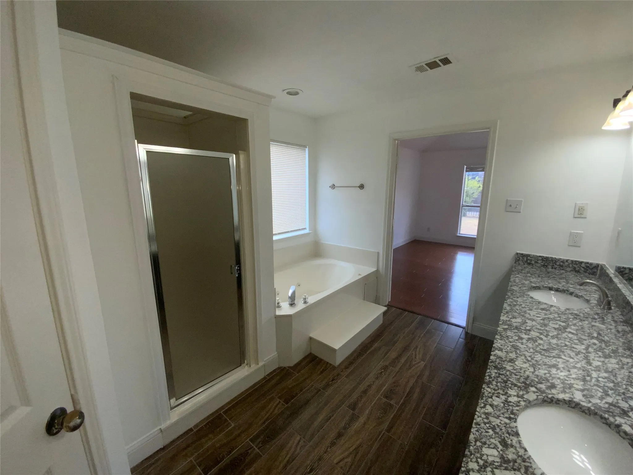Bathroom featuring wood-finish tile flooring, dual vanity with stone countertops, a built-in garden tub, and a separate shower enclosure