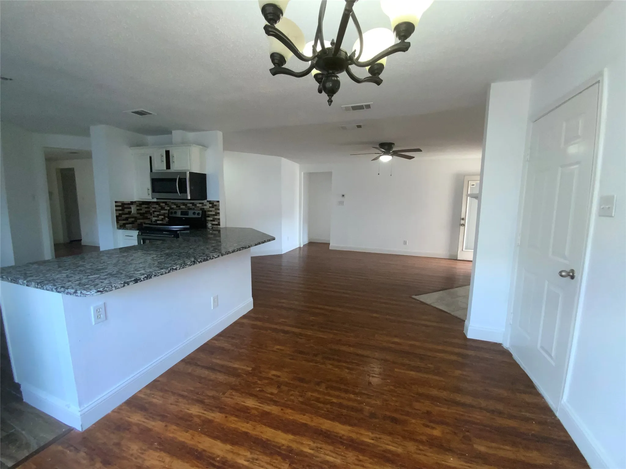 Open-concept interior featuring wood-finish flooring, a kitchen island with a stone-finish countertop, and white cabinetry
