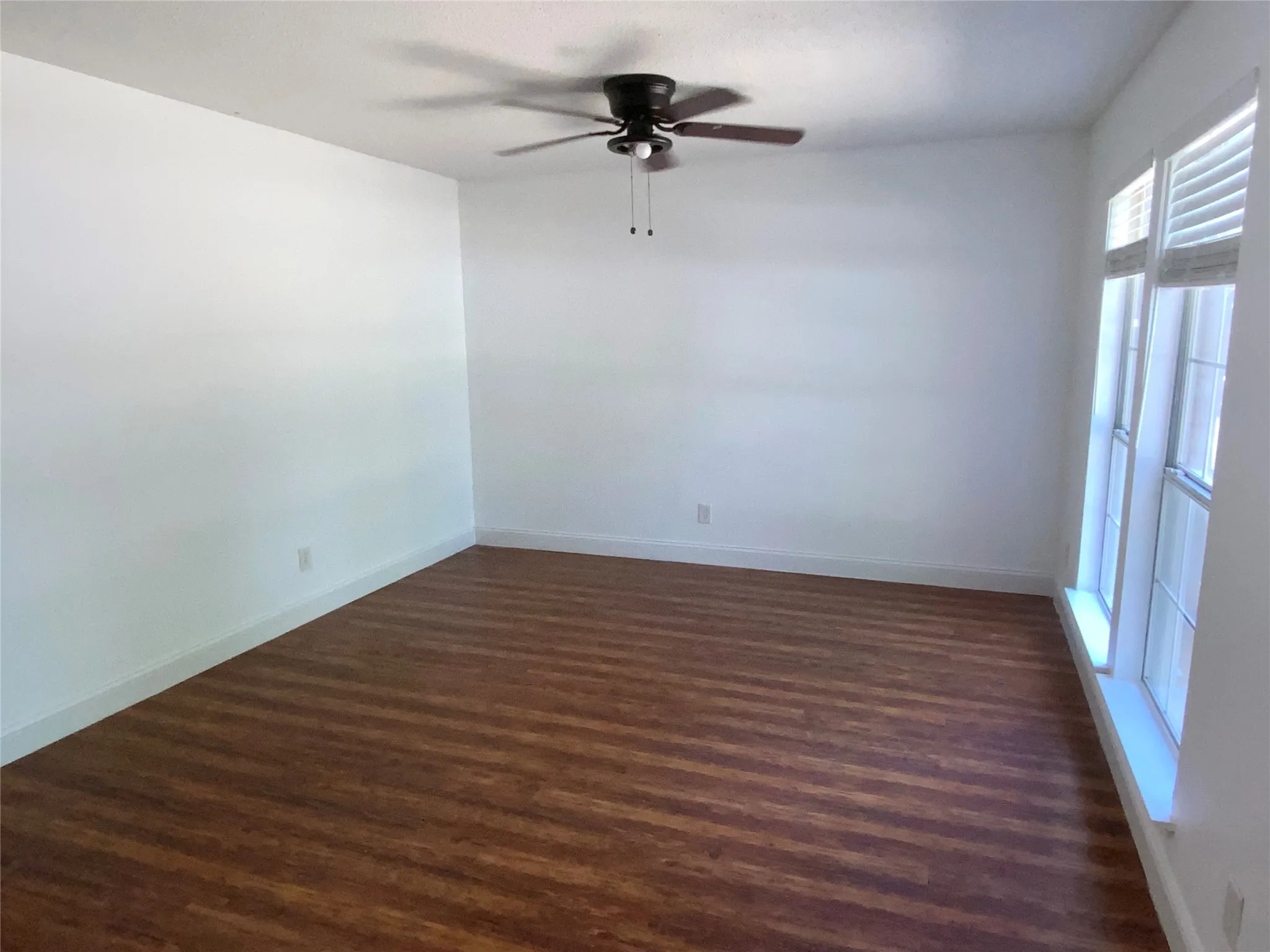 Spacious room featuring wood-finish flooring, white walls, and a ceiling fan