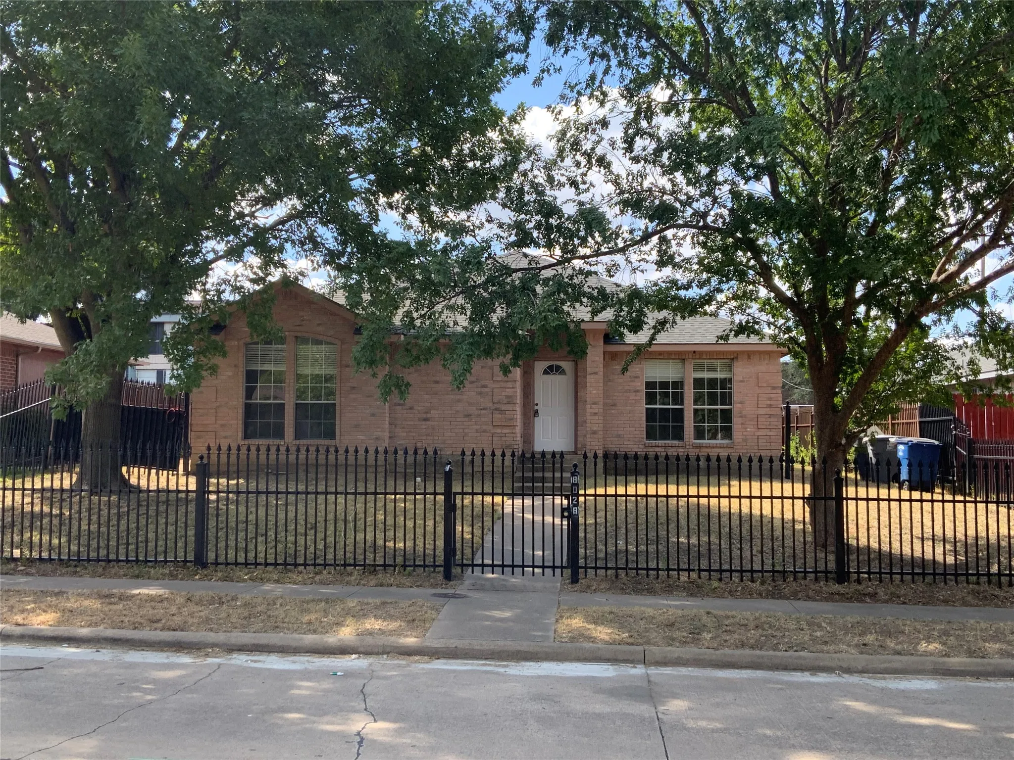 Brick exterior residence featuring a front entry door, bay window, and a black wrought iron fence