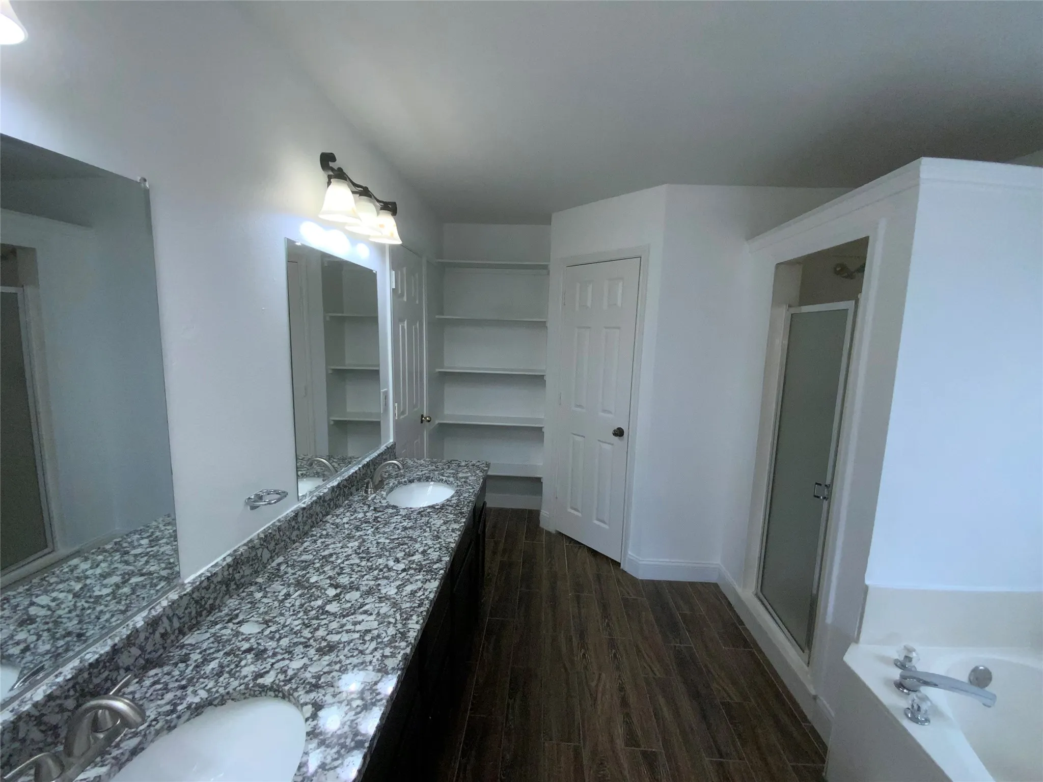Dual vanity with granite countertop, wood-finish flooring, built-in shelving, glass-enclosed shower, and built-in bathtub