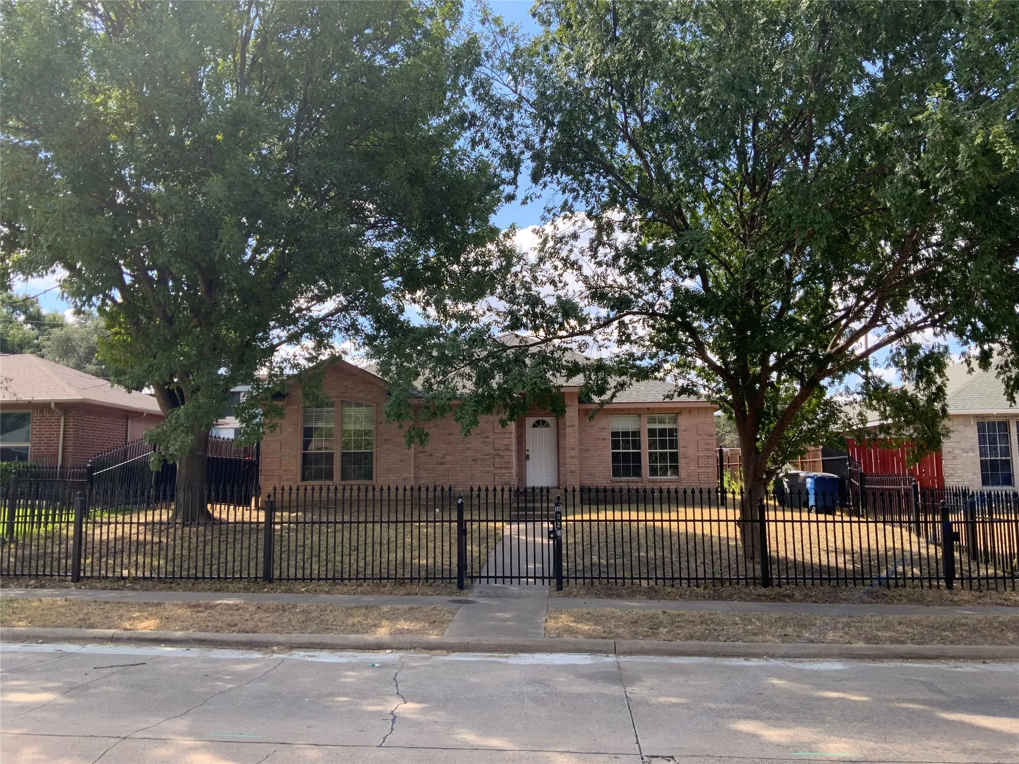 Brick exterior residence featuring a black wrought iron fence with a gate, mature trees, and multiple windows
