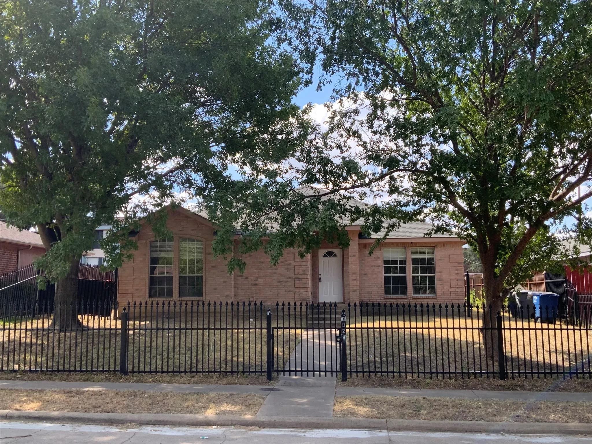 Brick exterior residence featuring a gabled roofline, multiple windows with white trim, and a black wrought iron fence