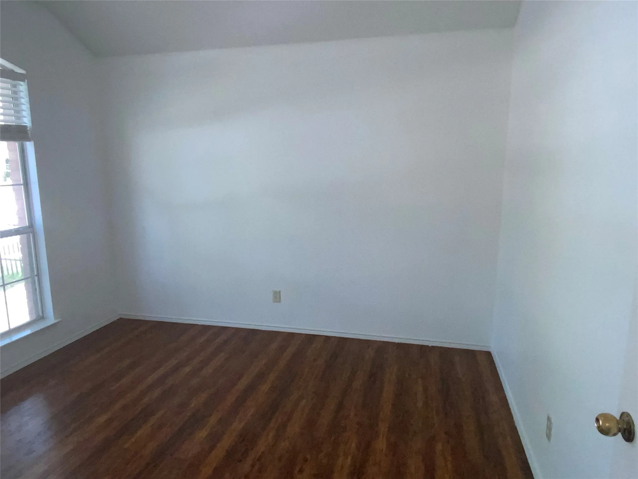 Room featuring wood-finish flooring, white walls, and a window with horizontal blinds