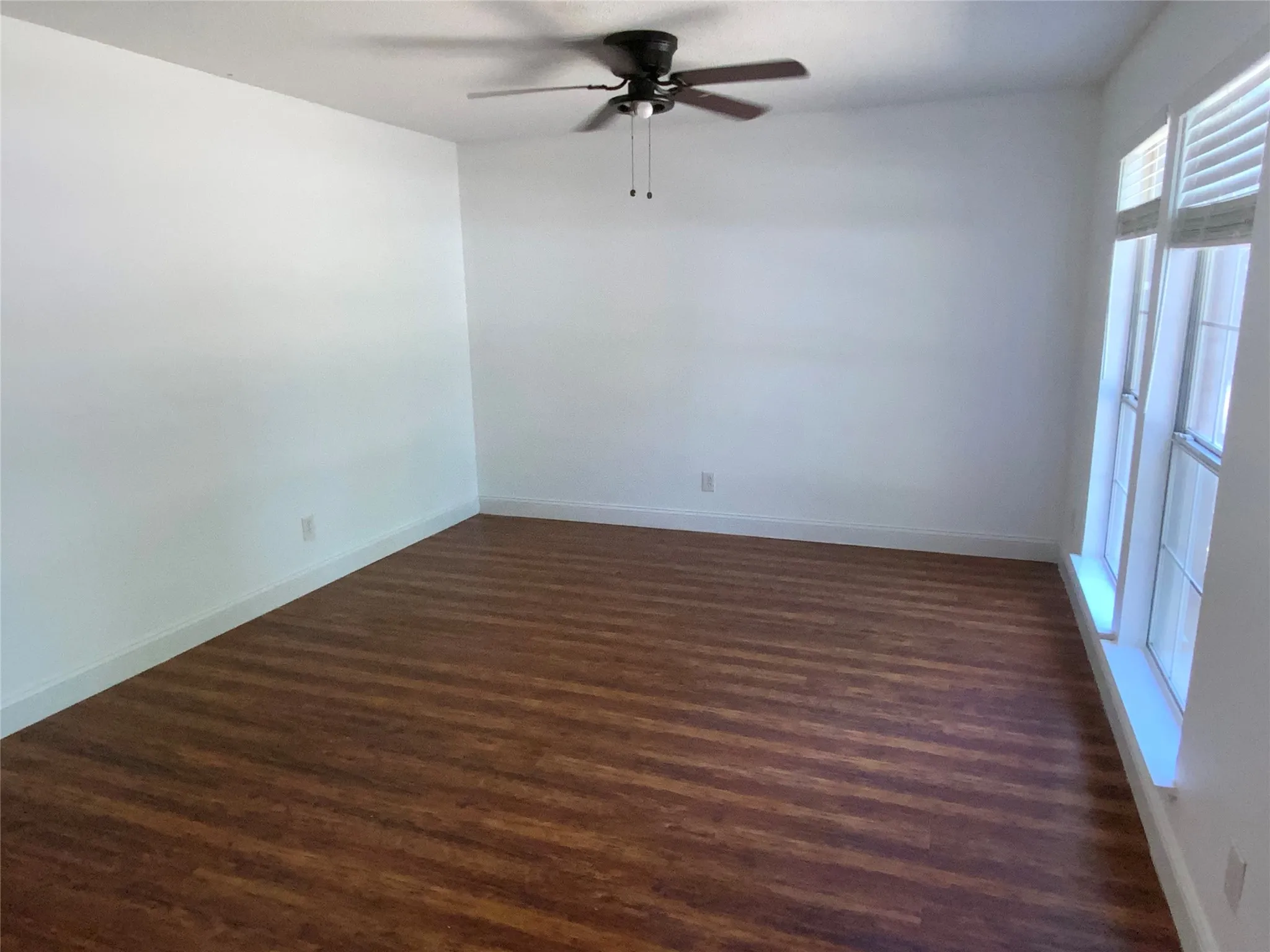 Spacious room featuring wood-finish flooring, a ceiling fan, and large windows with blinds