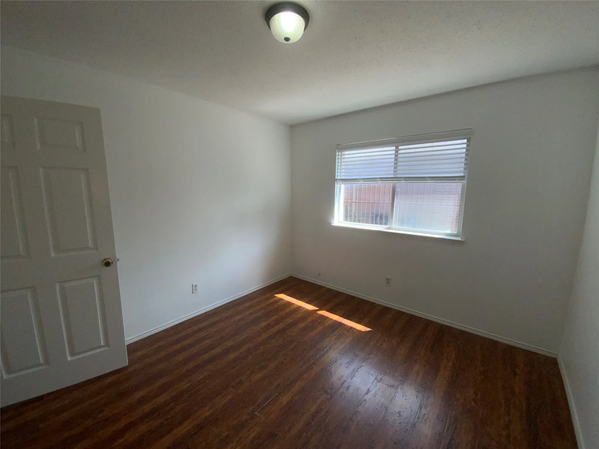 Wood-finish flooring, white walls, and a window with horizontal blinds