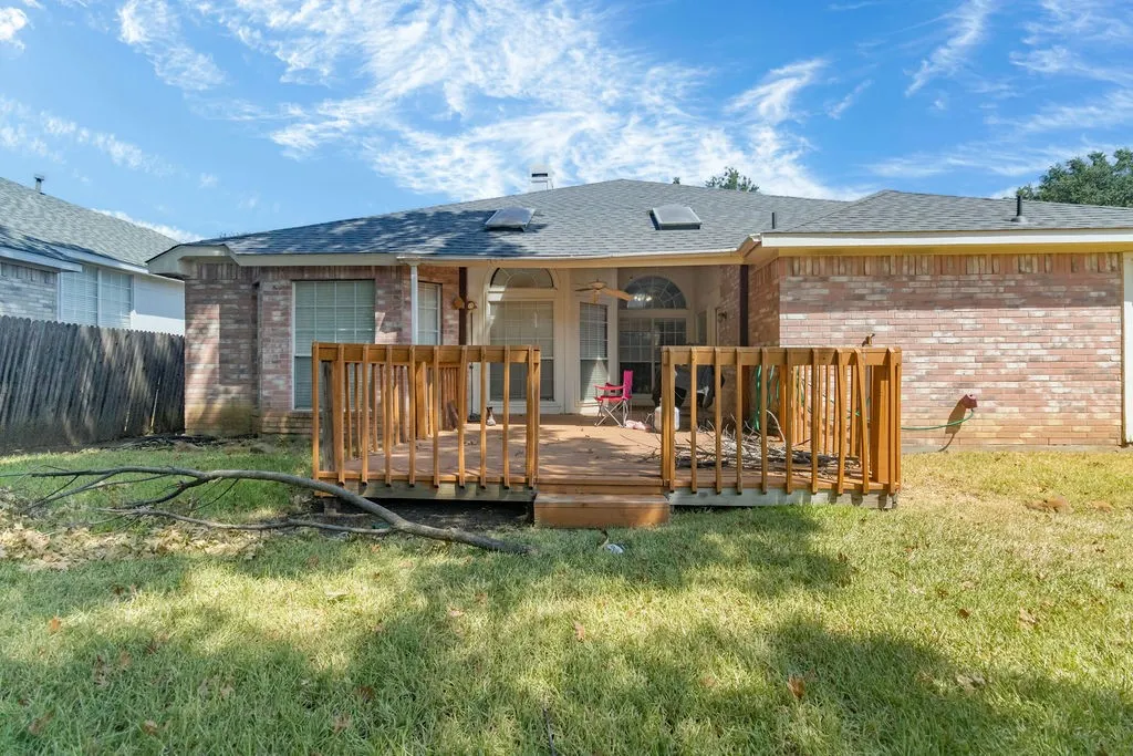 Brick exterior featuring a wood deck and a shingled roof with skylights