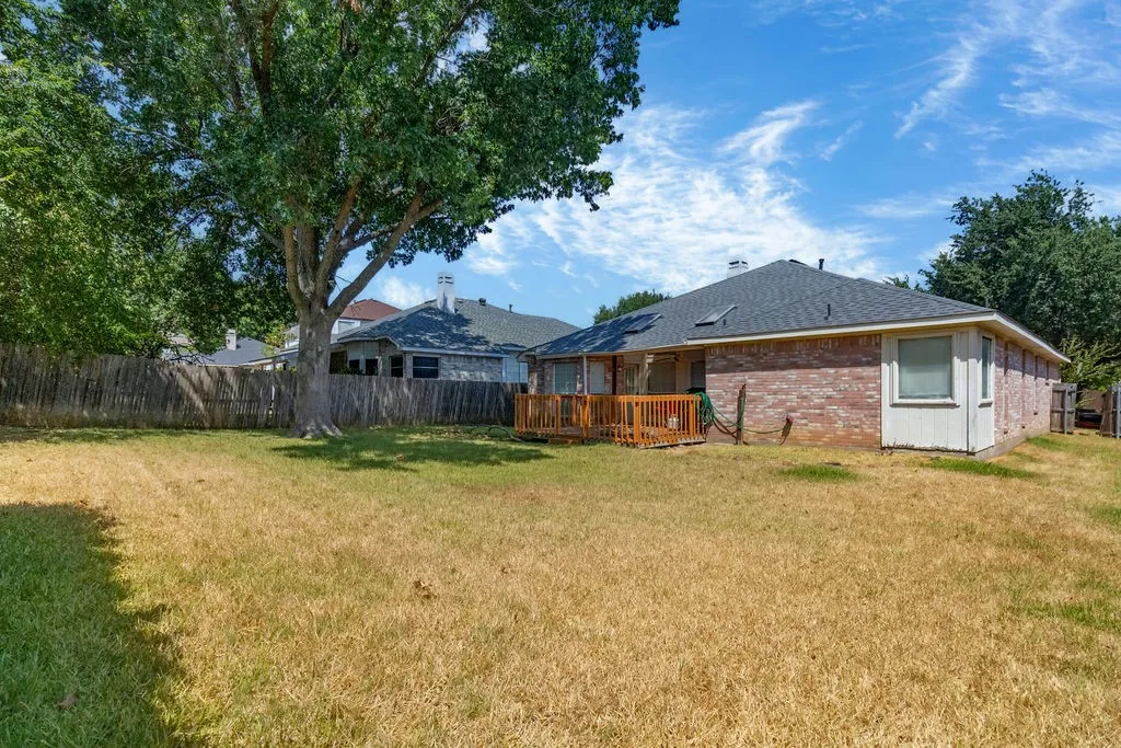 Expansive backyard featuring a mature shade tree, privacy fencing, and a wood deck