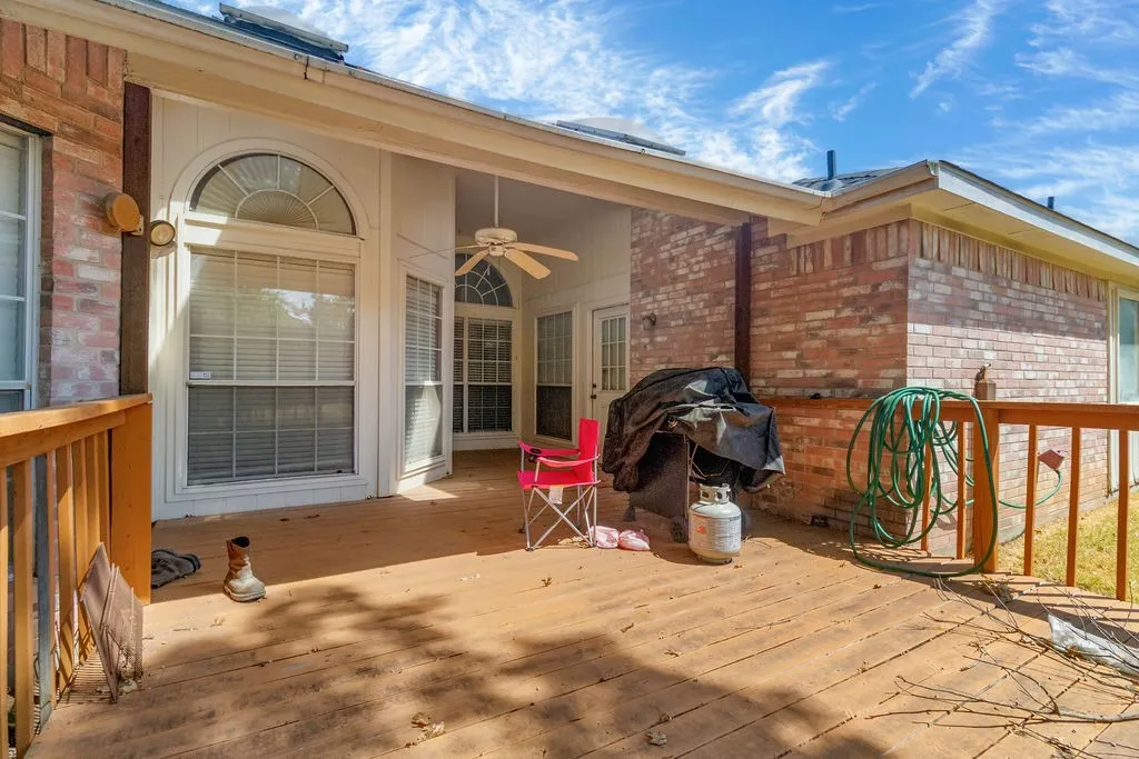 Expansive wood-finish deck with brick exterior, covered patio, arched window, and ceiling fan