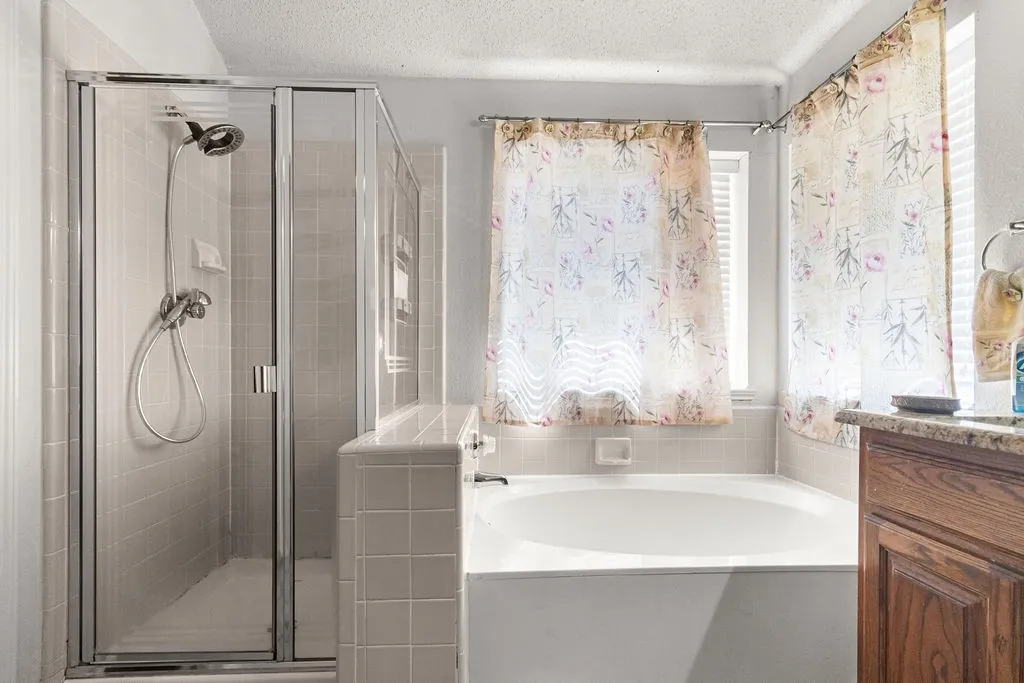 Tiled shower enclosure with a glass door, built-in bathtub, and a wood-finish vanity with a stone-finish countertop