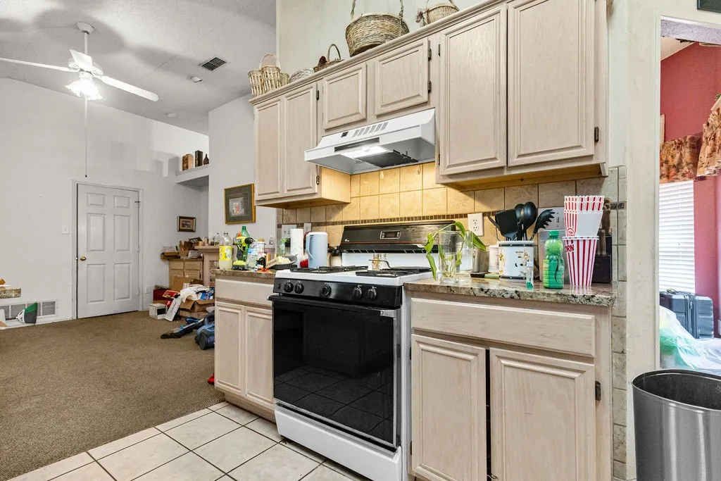 Kitchen with light wood-finish cabinetry, a tile backsplash, and a stone-finish countertop