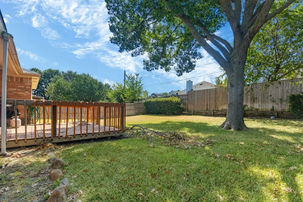 Expansive backyard featuring a wood deck, manicured lawn, and mature trees
