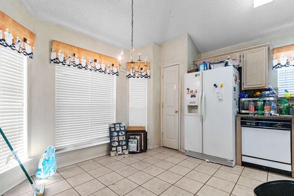 Tiled flooring with a multi-light chandelier, a white side-by-side refrigerator, and upper cabinetry