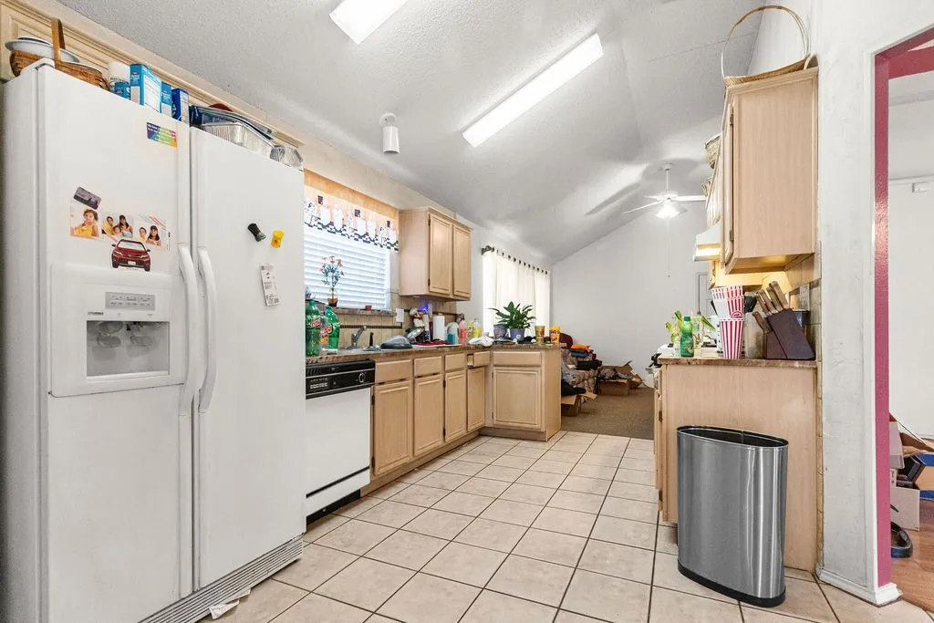 Kitchen featuring tile flooring, wood-finish cabinetry, a white side-by-side refrigerator, a white dishwasher, and vaulted ceilings