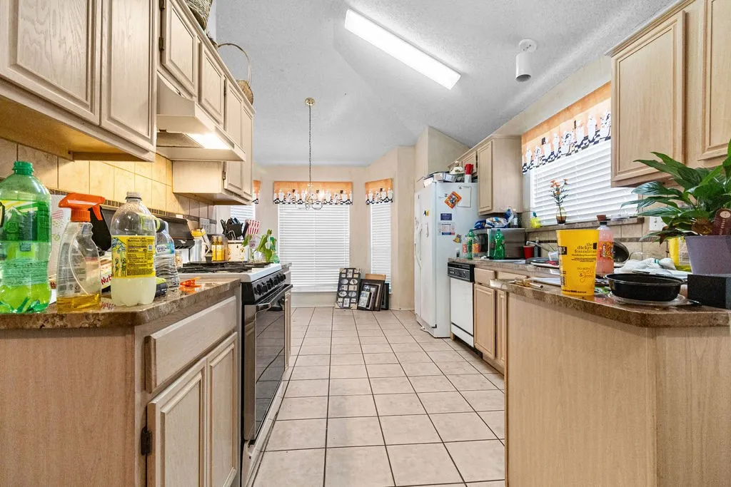 Kitchen featuring light wood-finish cabinetry, tile flooring, stone-finish countertops, and a full suite of appliances