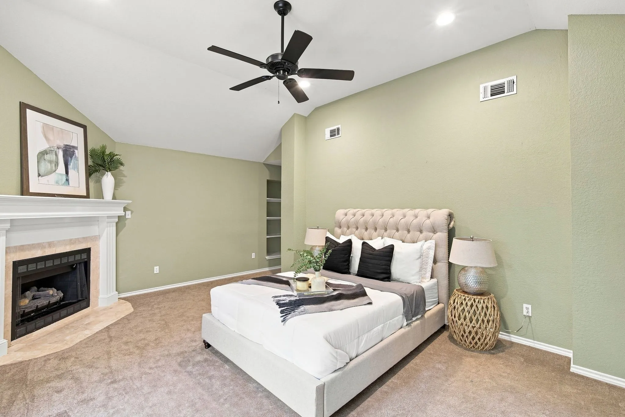 Spacious primary room with vaulted ceilings and a charming corner fireplace with a white mantel and tile surround.