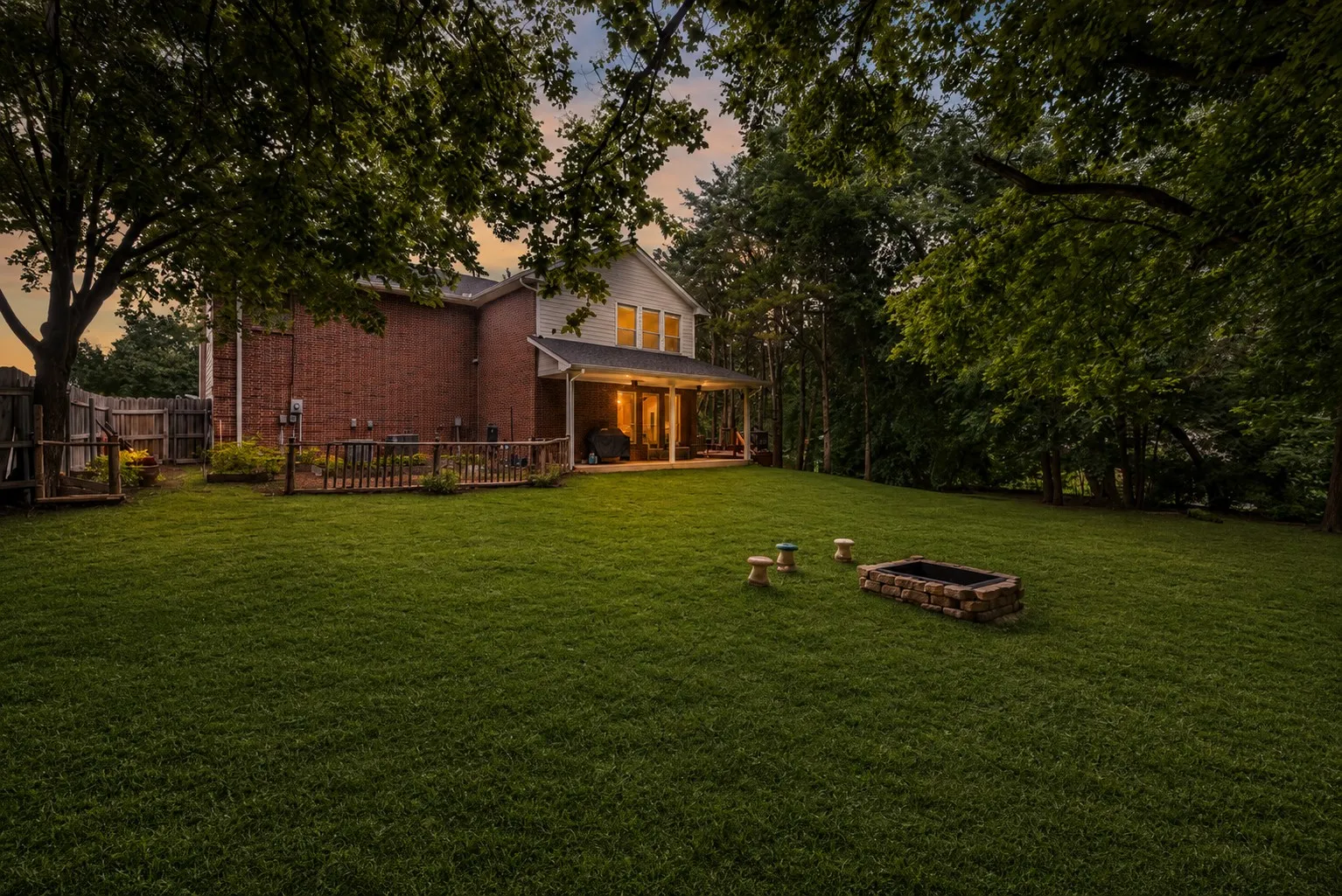 Spacious, tree-lined backyard with a covered patio, expansive lawn, and fire pit—perfect for relaxing, entertaining, or enjoying the outdoors.