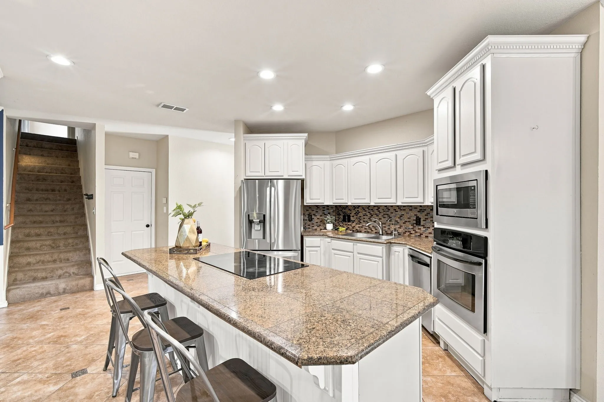 Chef-ready kitchen featuring white cabinetry, a center island with a cooktop, and granite counters.