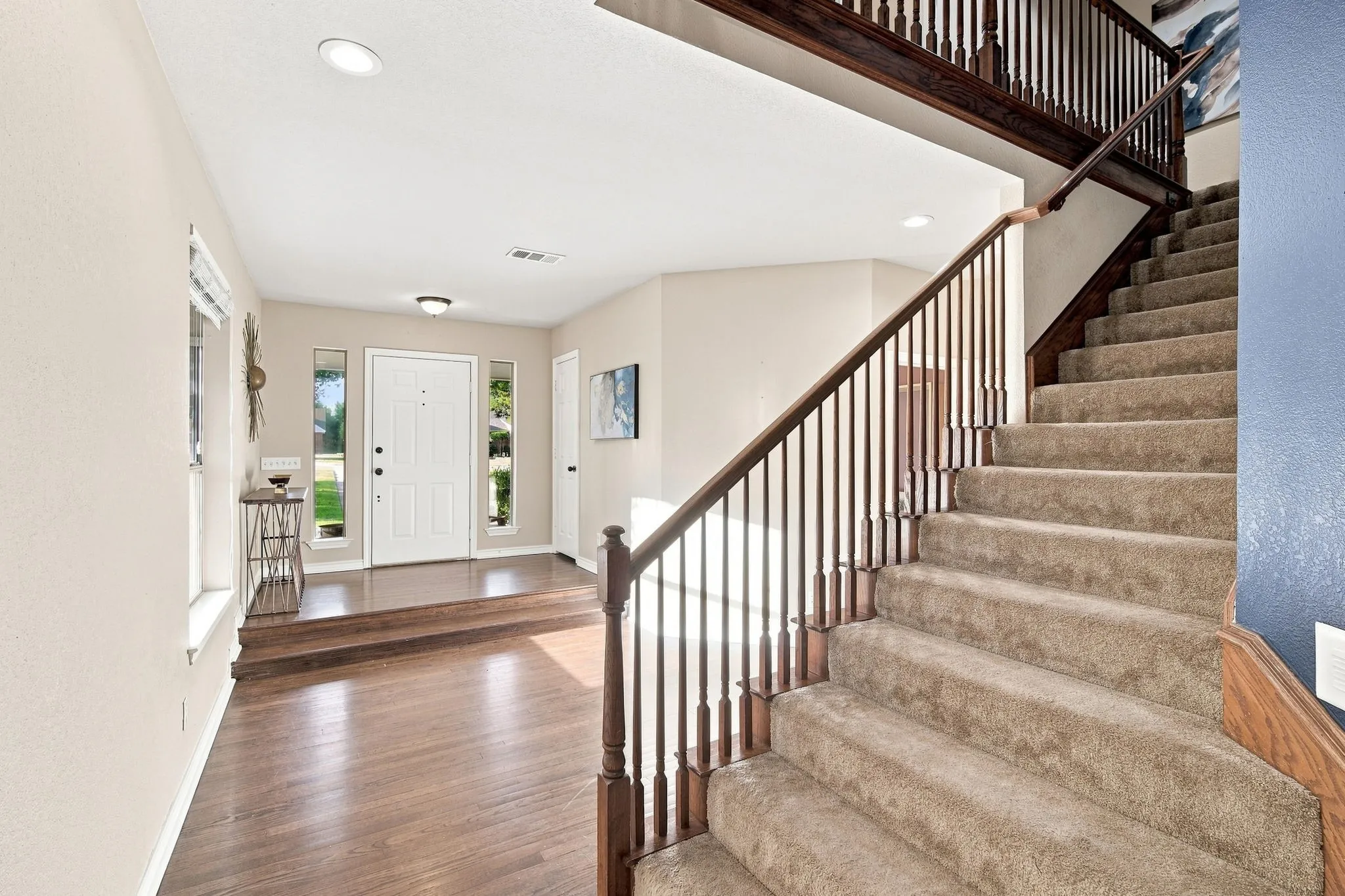 Step inside to a bright entryway with rich wood-look flooring, an elegant paneled front door with sidelights, and a staircase with a warm wood handrail.